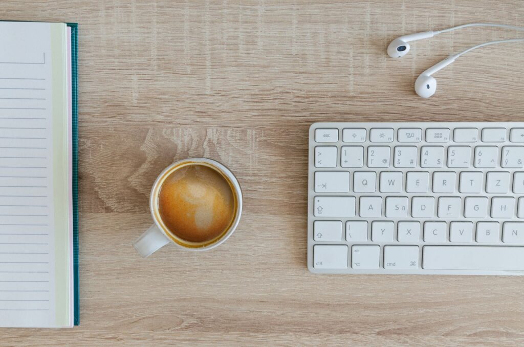 A tidy workspace with a notebook, coffee cup, keyboard, and earphones on a wooden desk.