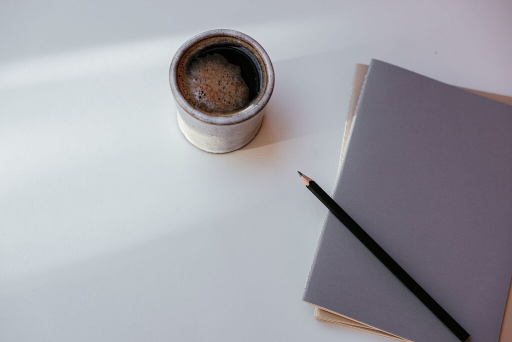 A cozy coffee mug with a notebook and pencil on a clean, minimalist desk.